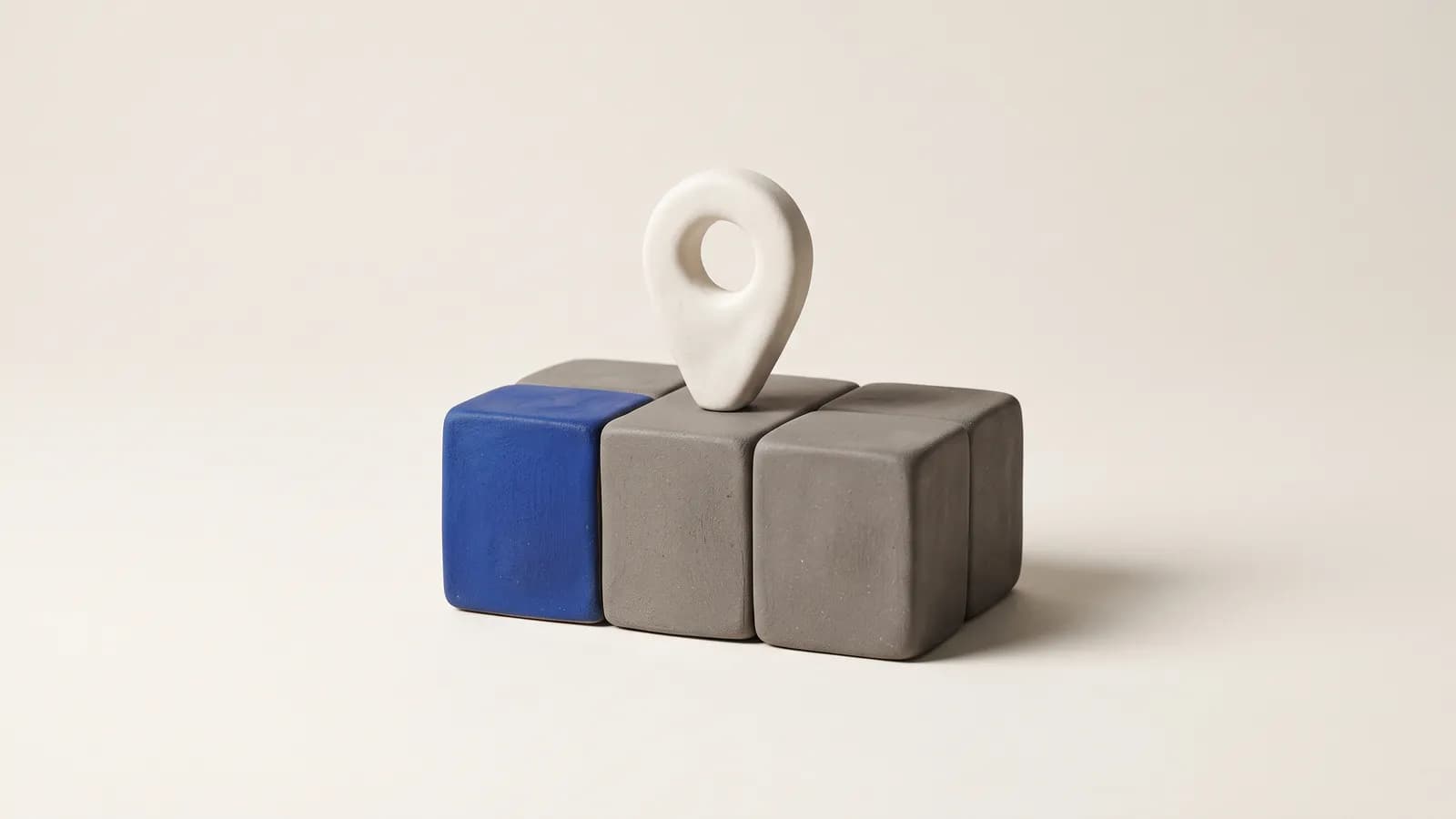A matte clay map pin standing on a small clay calendar block with one cobalt square, on a warm off-white background