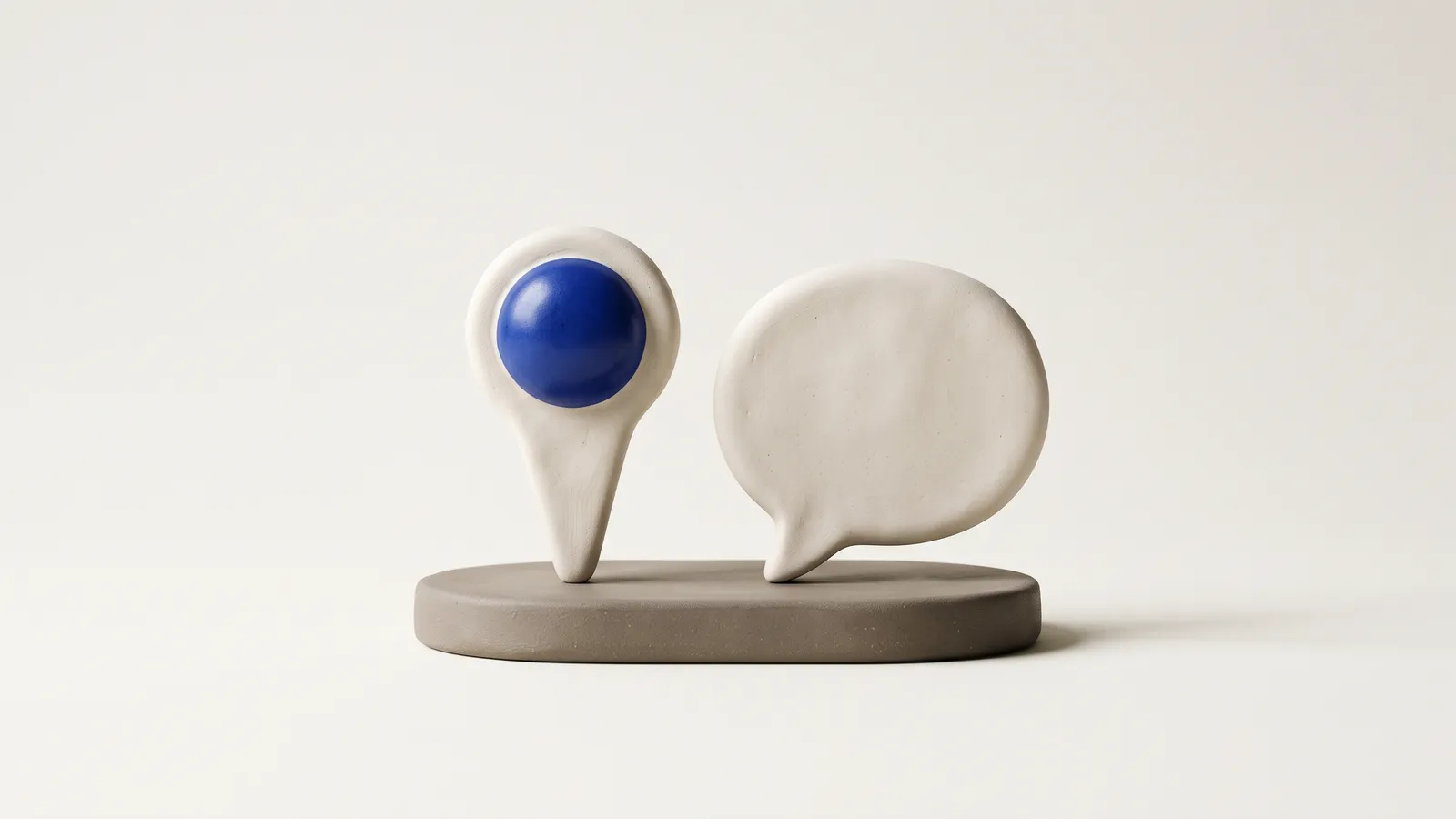 Two matte clay objects side by side, a map pin and a speech bubble with a small cobalt accent, on a warm off-white background