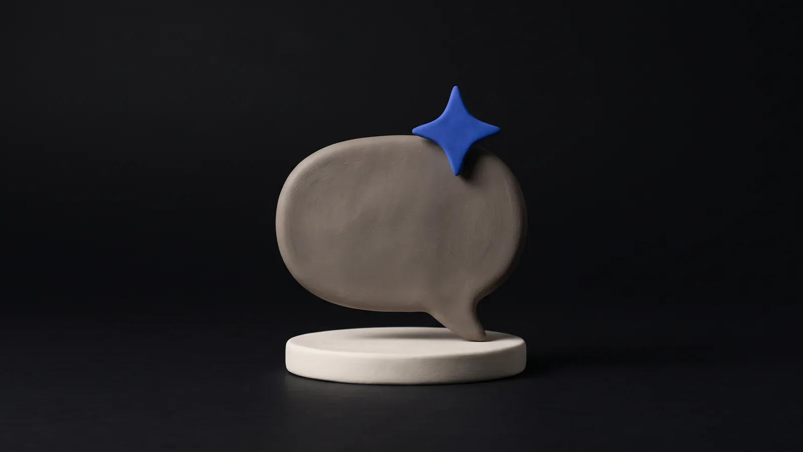 A matte clay speech bubble with a small cobalt spark resting on top, on a near-black background
